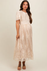 woman wearing a cream embroidered maternity maxi dress with short puff sleeves and a flowing skirt, highlighting her baby bump