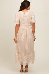woman wearing a beige maternity dress with sheer sleeves and floral embroidery, showing the back view