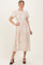 woman wearing a beige midi dress with short sleeves and floral embroidery, posing with one hand on her hip