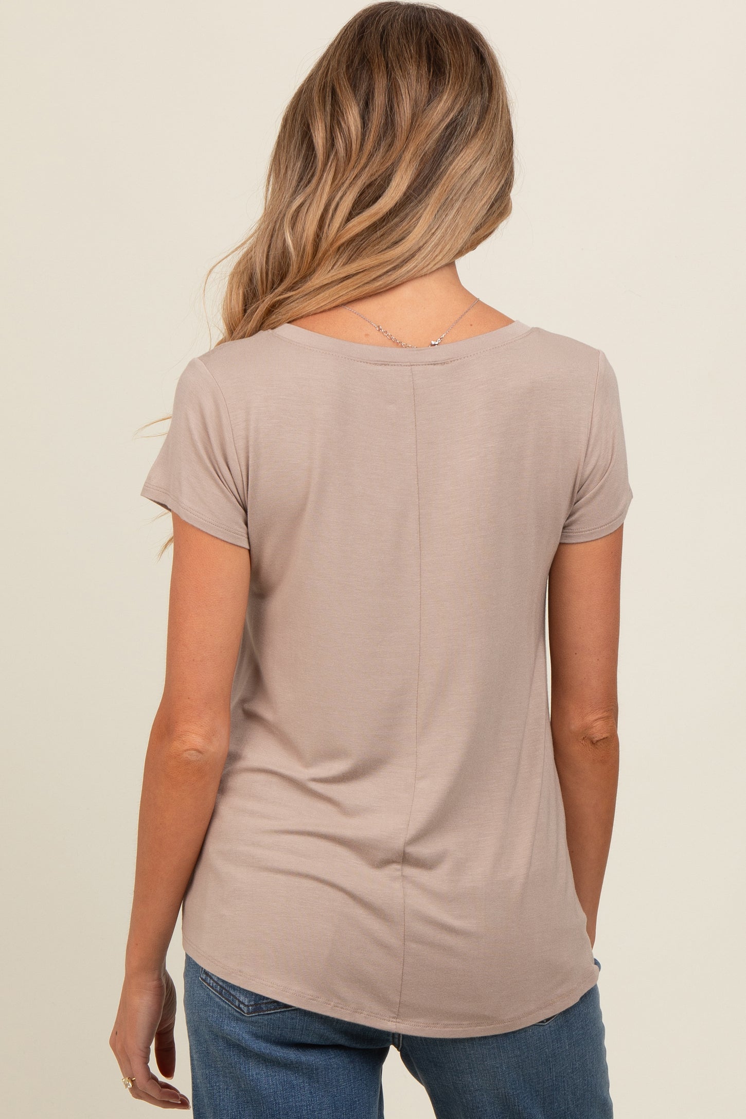 woman wearing a taupe short sleeve maternity top, seen from the back, paired with blue jeans