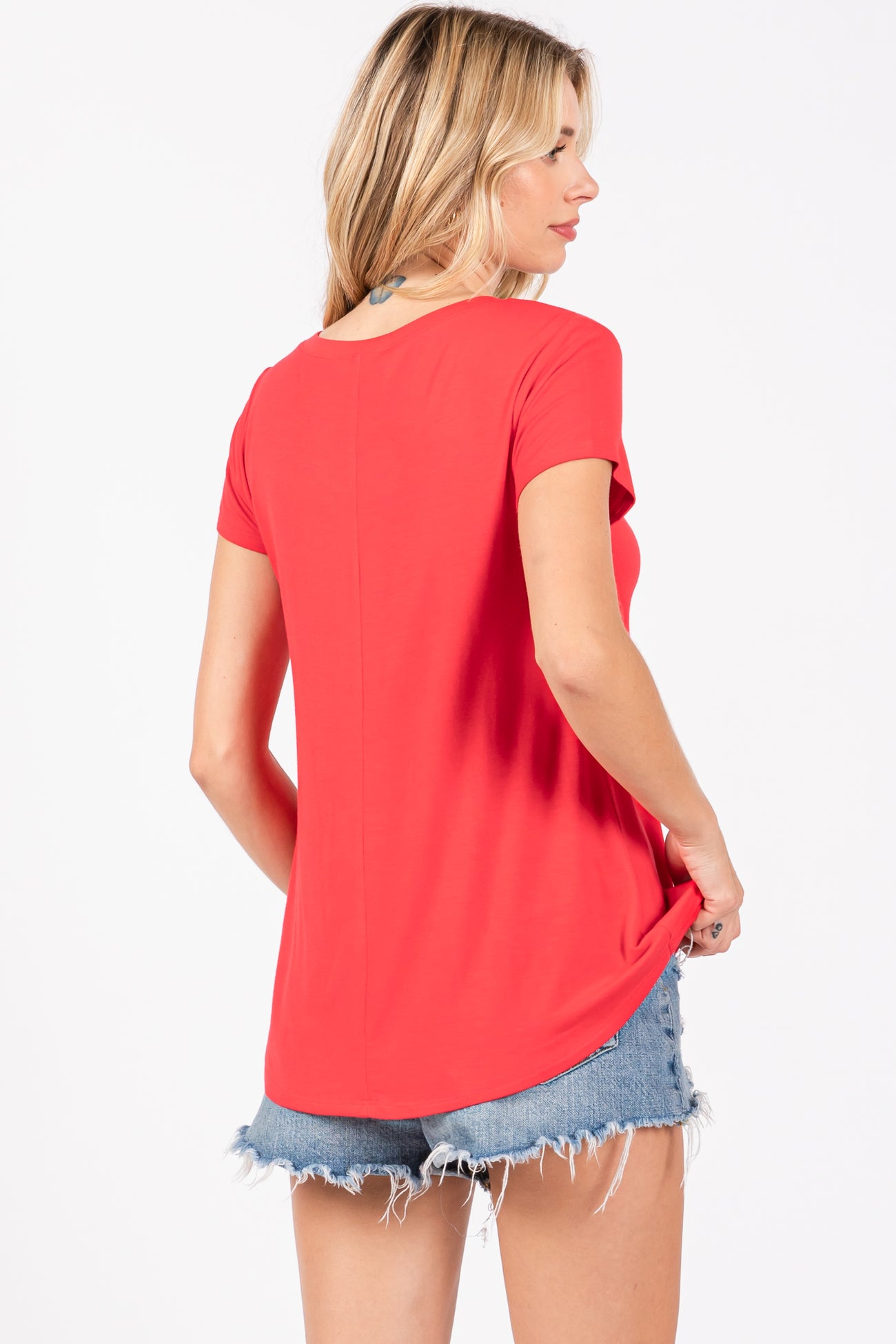 woman wearing a red short sleeve top with a rounded hem and distressed denim shorts