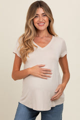 woman wearing a beige short sleeve maternity top and holding her baby bump