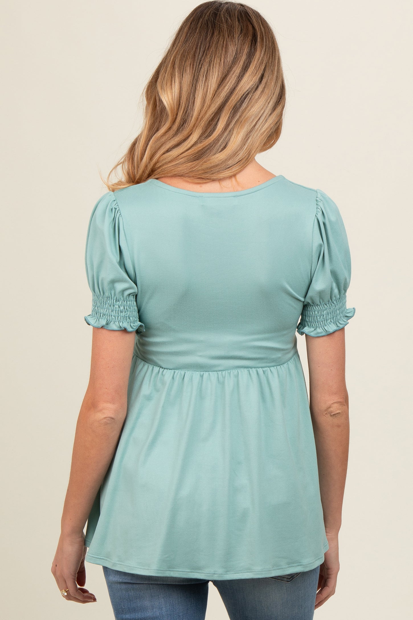 woman wearing a mint green short sleeve maternity top with smocked details at the sleeves and back