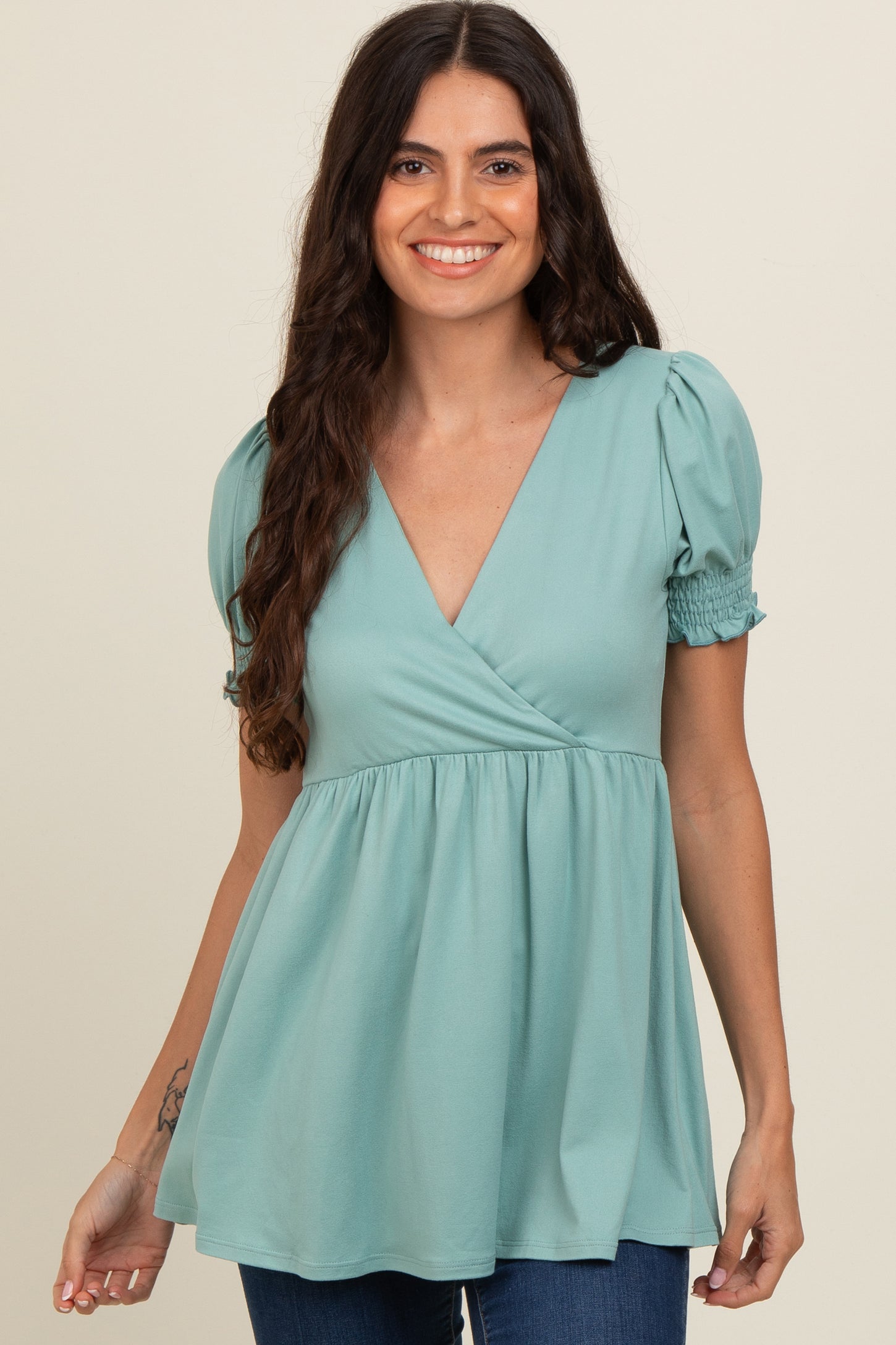woman wearing a teal puff sleeve top with a v-neck and gathered waist, smiling at the camera