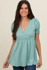 woman wearing a teal puff sleeve top with a v-neck and gathered waist, smiling at the camera