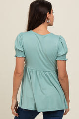 woman wearing a teal smocked back top with puff sleeves and a flared hem