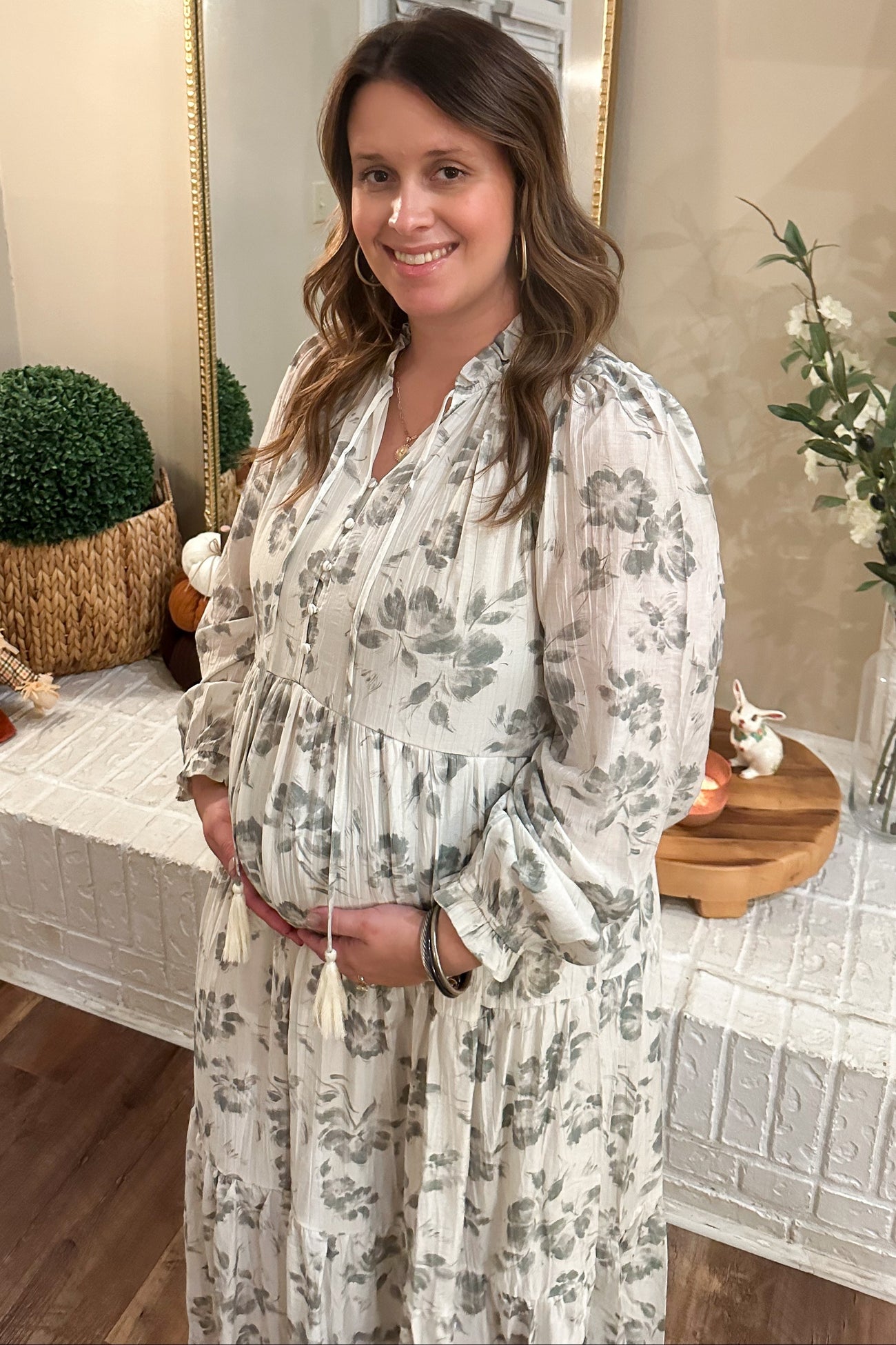 woman wearing a light grey floral maternity dress and holding her baby bump