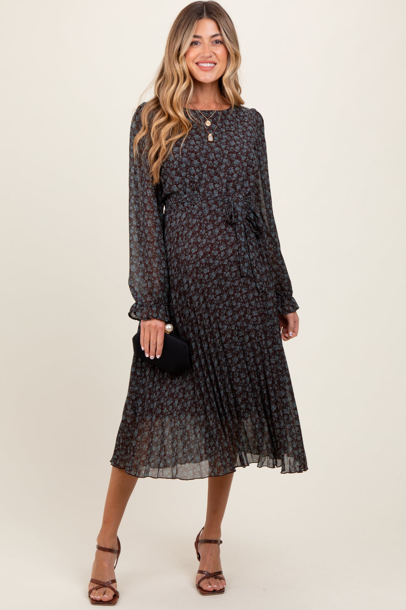 woman wearing a dark floral maternity dress with long sleeves and a tied waist, holding a small black clutch