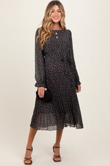 woman wearing a dark floral maternity dress with long sleeves and a tied waist, holding a small black clutch