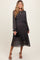 woman wearing a dark floral maternity dress with long sleeves and a tied waist, holding a small black clutch