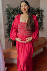 woman wearing a bright pink maternity maxi dress with smocked bodice and puff sleeves, holding her baby bump