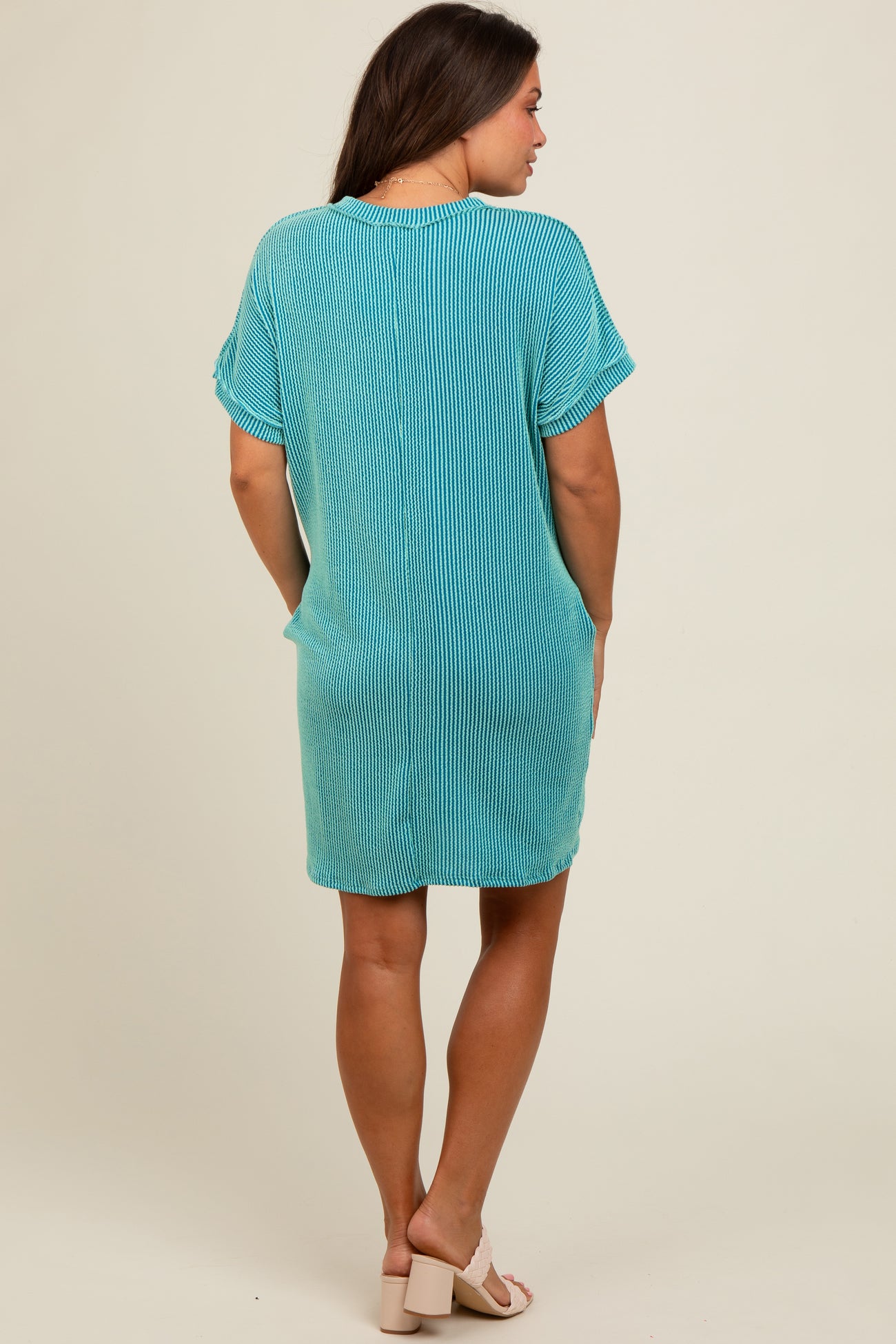woman wearing a striped teal maternity dress with short sleeves and pockets, showing a relaxed fit from the back