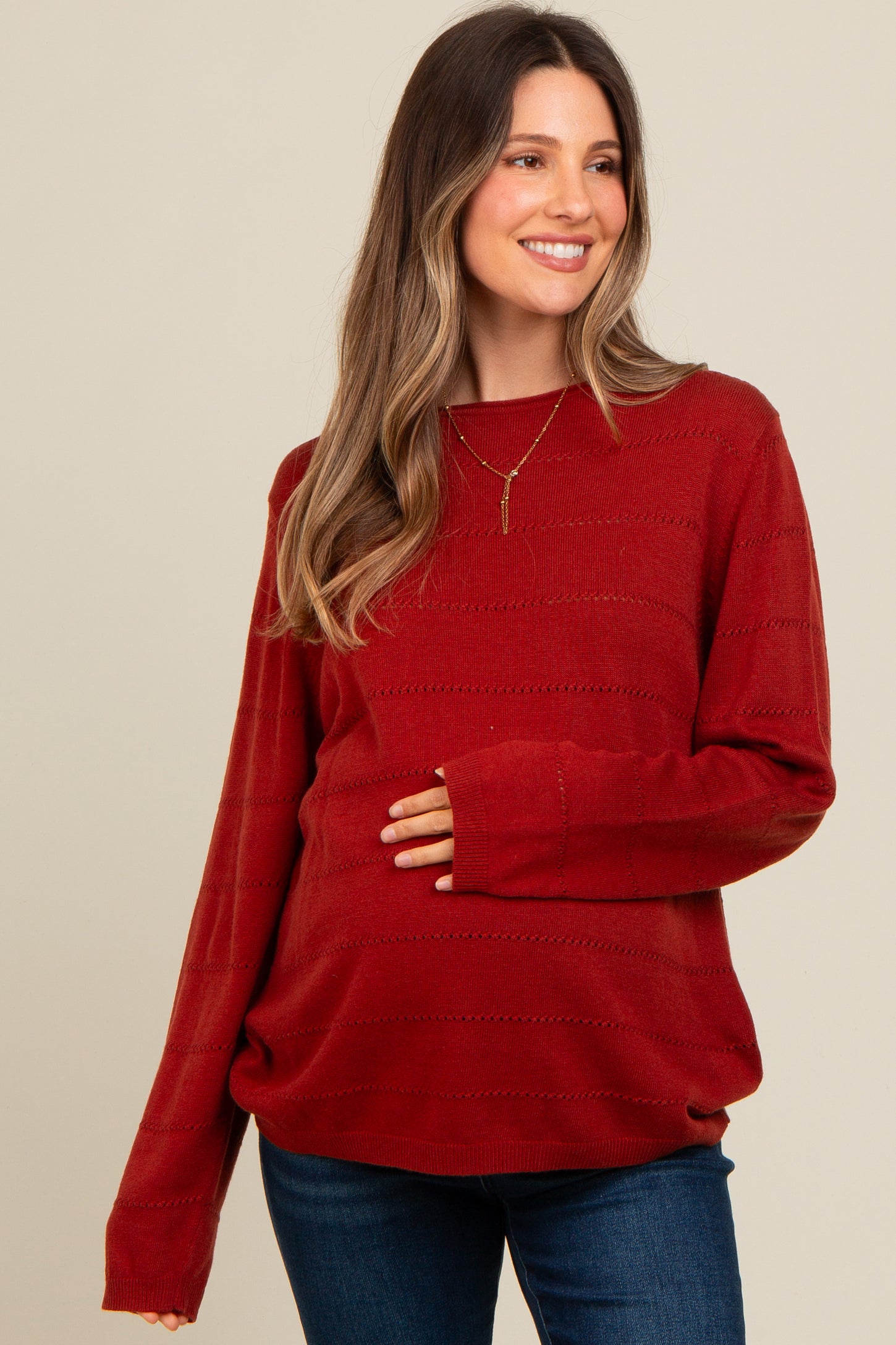 woman wearing a rust red maternity sweater with textured stripes and holding her baby bump