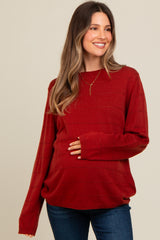 woman wearing a rust red maternity sweater with textured stripes and holding her baby bump