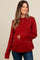 woman wearing a rust red maternity sweater with textured stripes and holding her baby bump