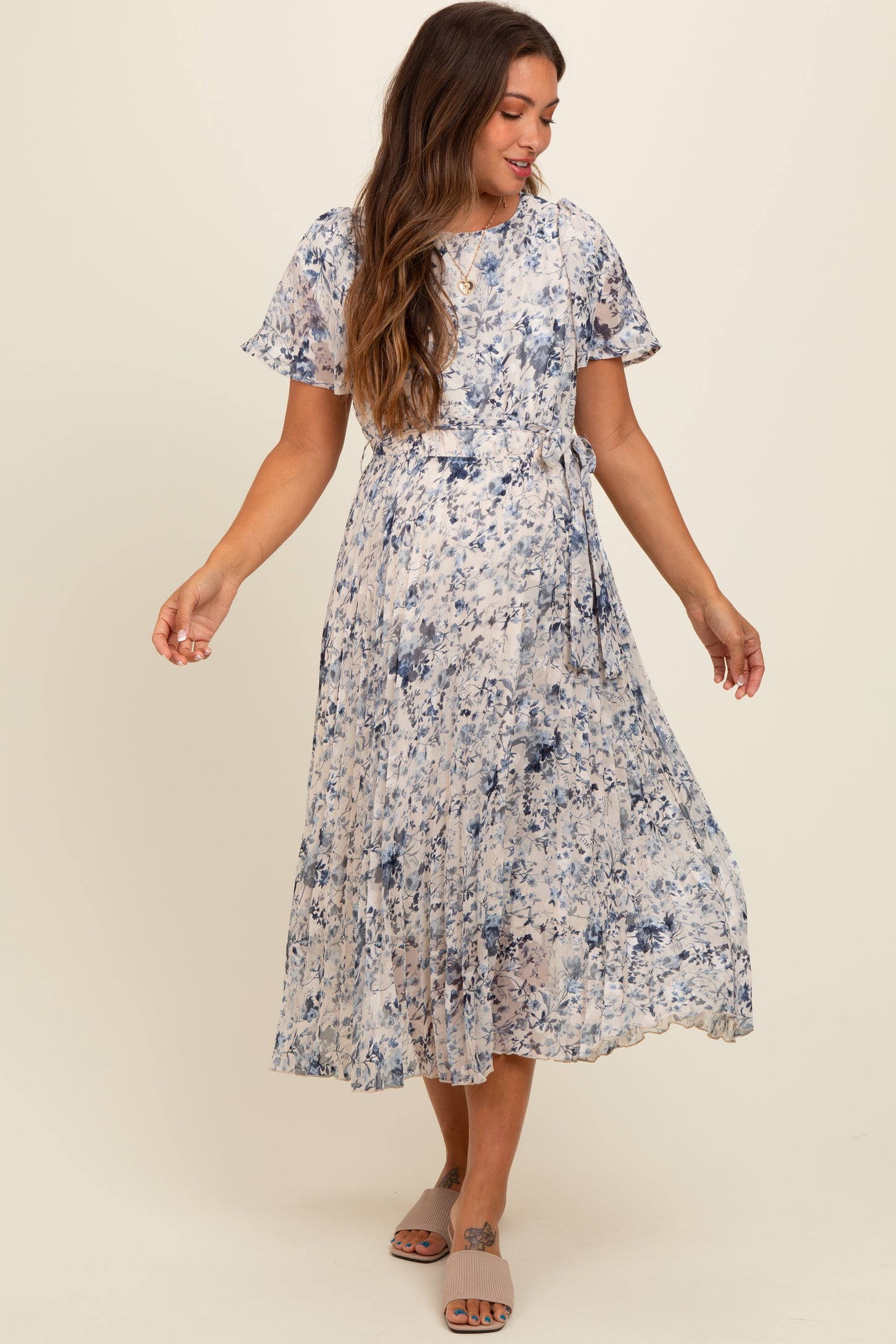 woman wearing a blue and cream floral maternity dress with short sleeves and a tie waist detail, smiling while posing