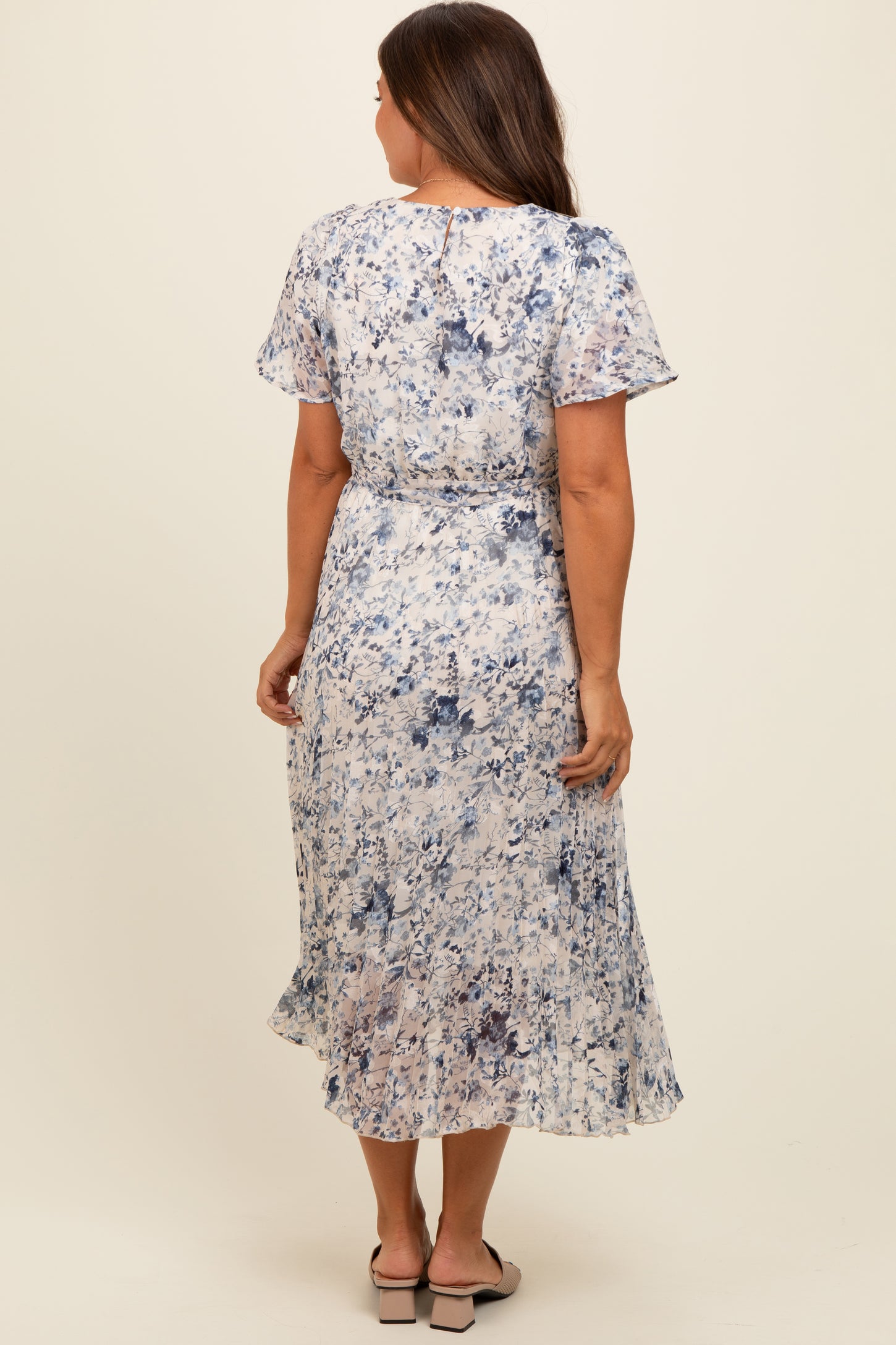 woman wearing a flowy floral print maternity dress with short sleeves and a cinched waist, standing with her back to the camera