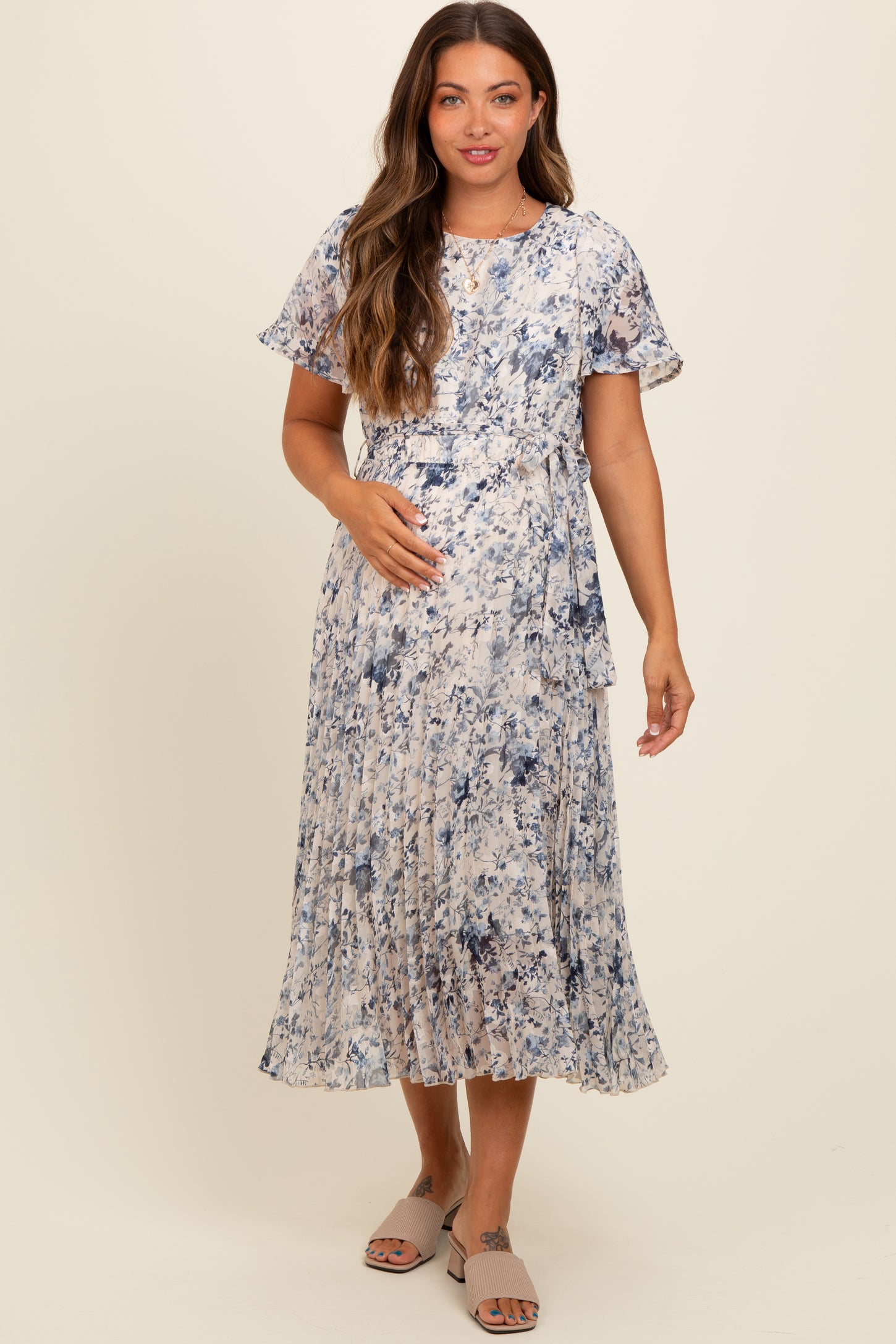 woman wearing a flowy floral maternity dress with short sleeves and a pleated skirt, holding her baby bump