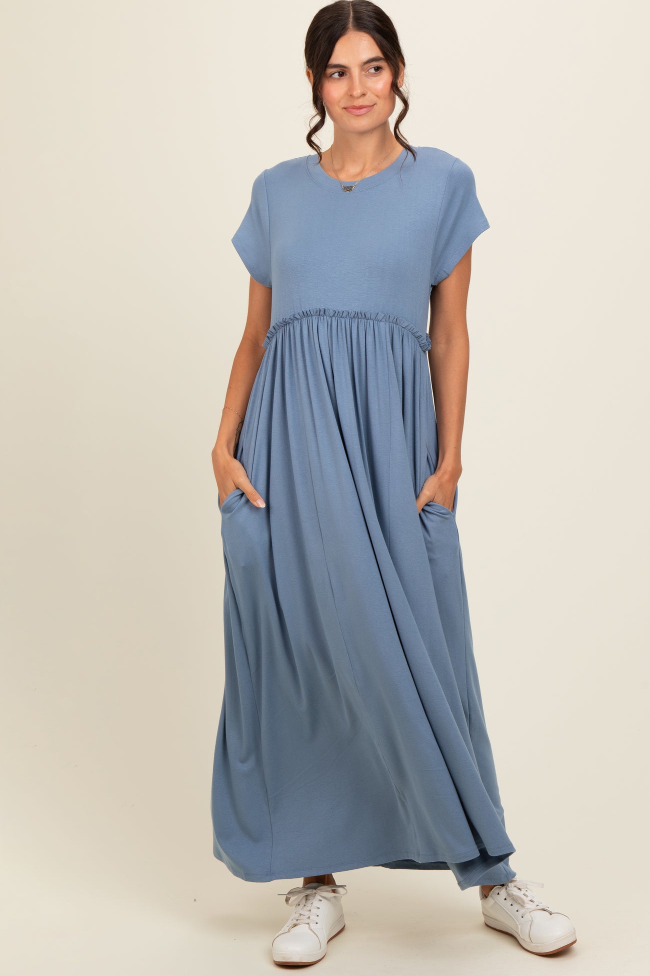 woman wearing a blue short sleeve maxi dress with a gathered waist and pockets, styled with white sneakers