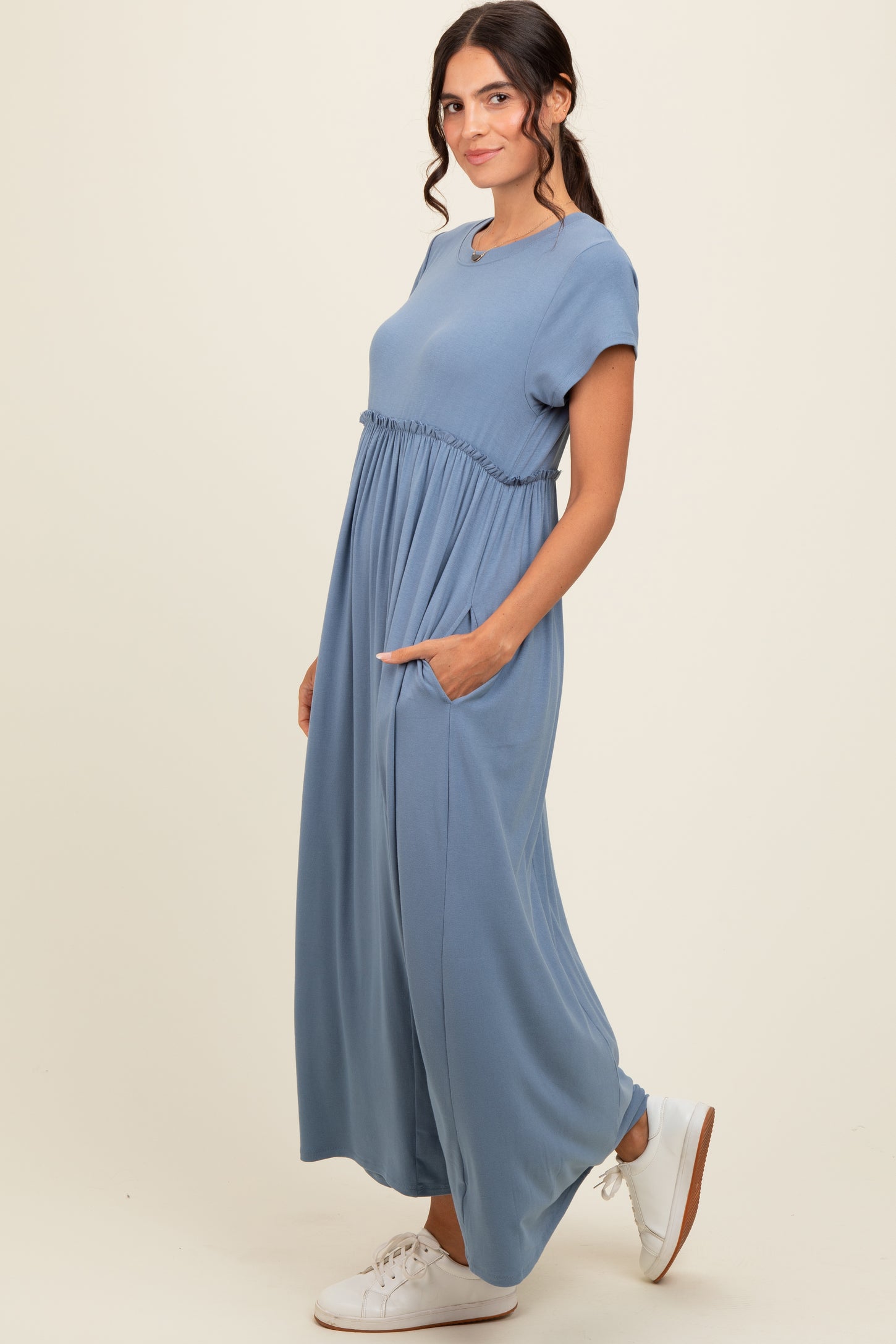 woman wearing a blue short sleeve maxi dress with an elastic waist and pockets, styled with white sneakers