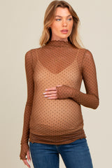woman wearing a brown polka dot maternity top with long sleeves and a mock neck, showing off her baby bump