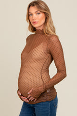 woman wearing a sheer brown polka dot maternity top and holding her baby bump
