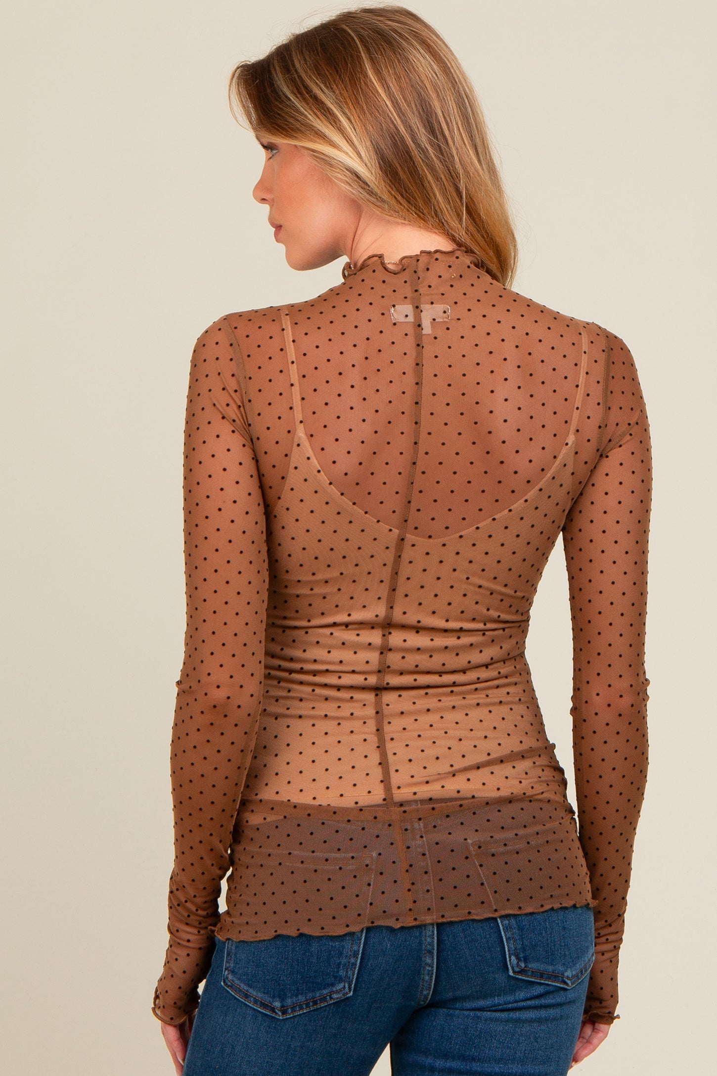 woman wearing a brown sheer maternity top with black polka dots and long sleeves, styled with a ruffled collar