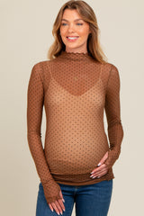 woman wearing a brown sheer maternity top with black polka dots and a ruffled neckline, holding her baby bump