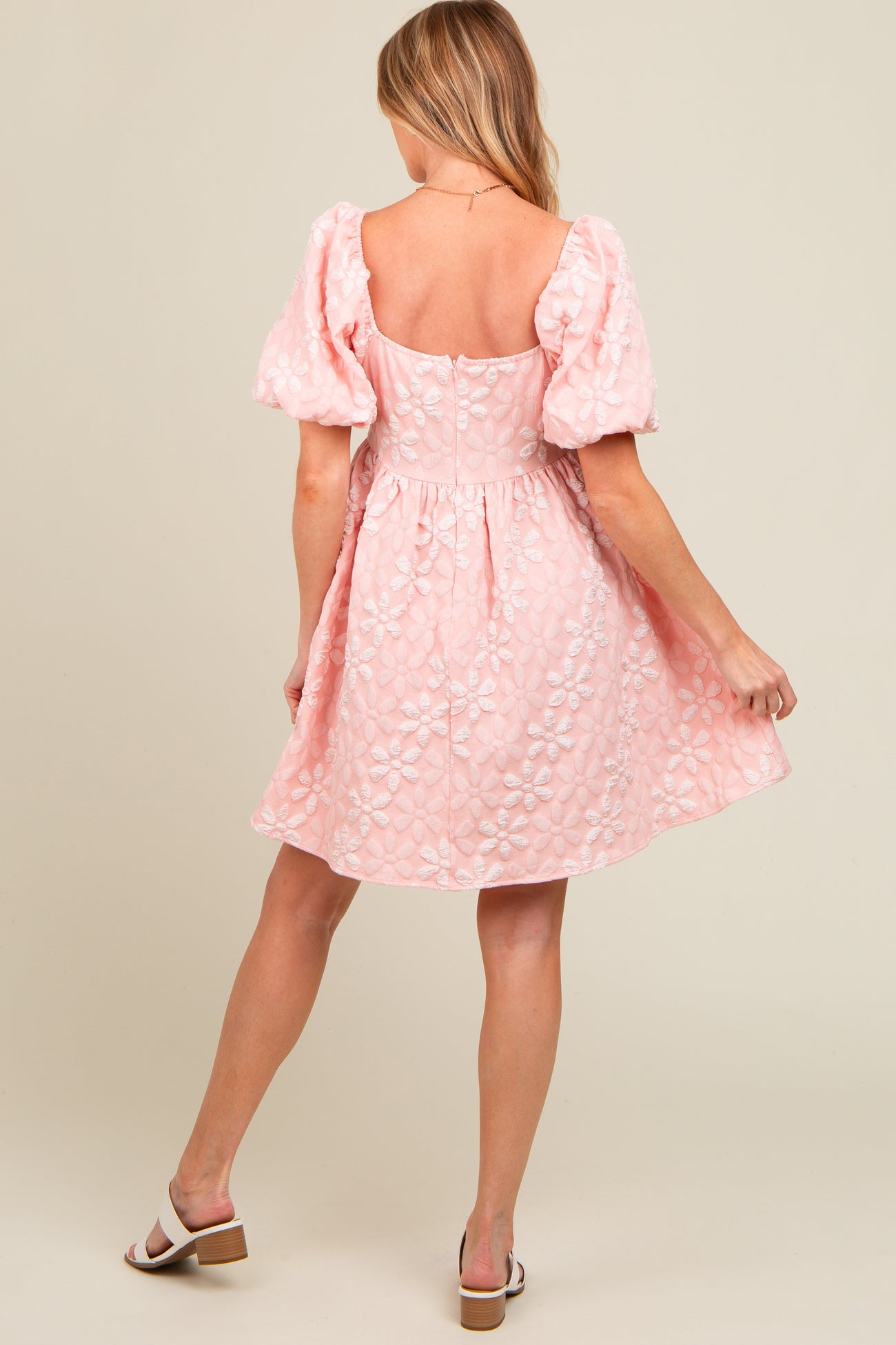 woman wearing a light pink maternity dress with puff sleeves and floral embroidery, showcasing a delicate a-line silhouette
