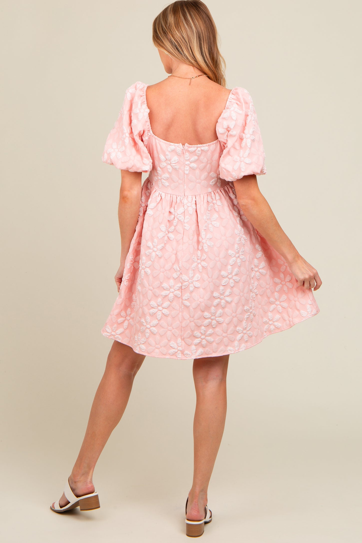 woman wearing a light pink maternity dress with puff sleeves and floral embroidery, showcasing a delicate a-line silhouette