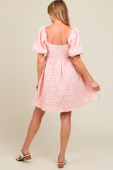 woman wearing a light pink maternity dress with puff sleeves and floral embroidery, showcasing a delicate a-line silhouette