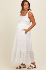woman wearing a white maternity maxi dress with tiered lace details and tie shoulder straps, holding her baby bump