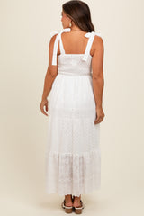 woman wearing a white maternity maxi dress with tie straps and eyelet details, showing her pregnant belly