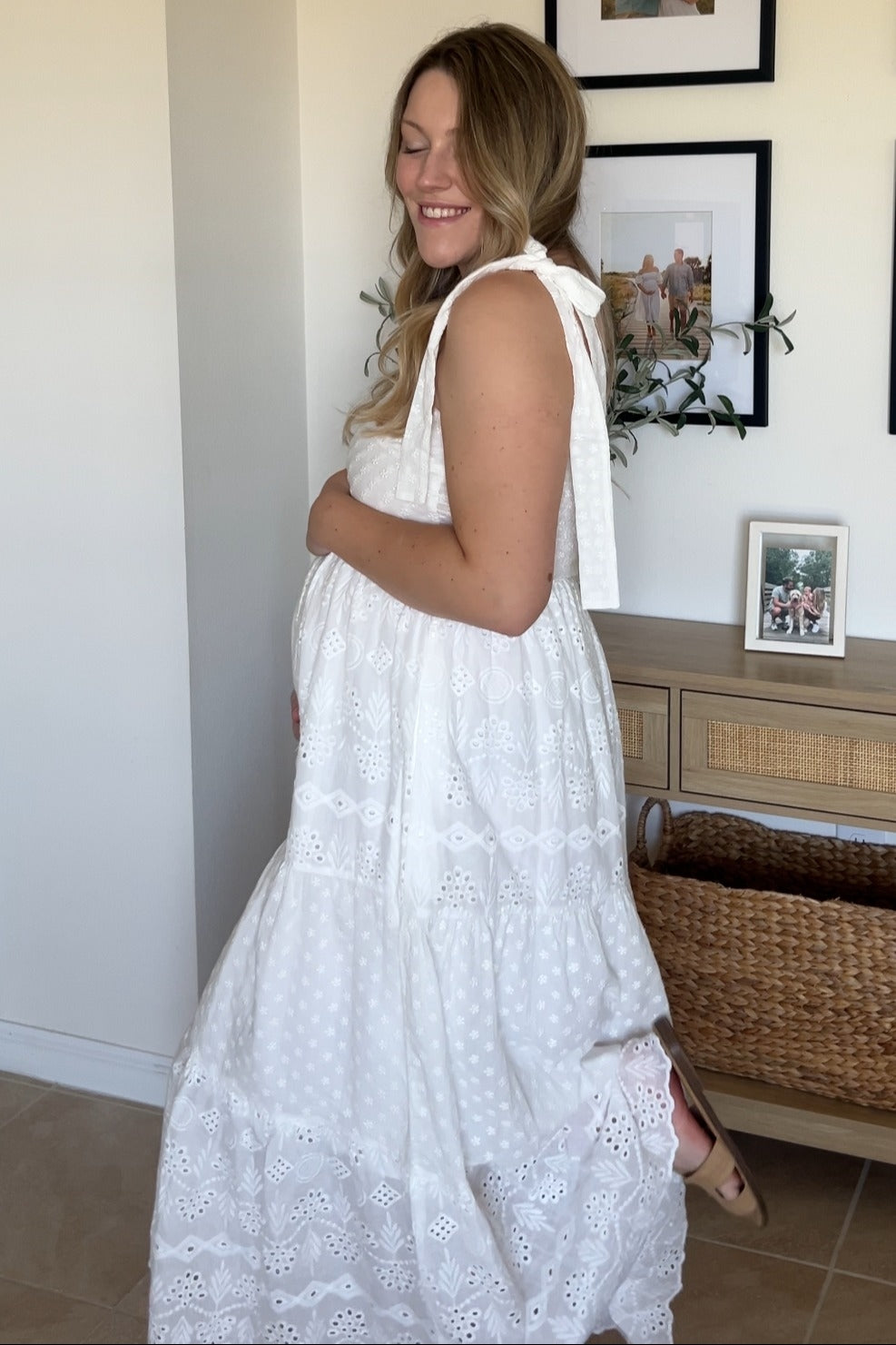 woman wearing a white eyelet tiered maternity dress and holding her baby bump