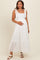 woman wearing a white maternity maxi dress with lace details and tie straps, holding her baby bump