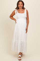 woman wearing a white maternity maxi dress with shoulder ties and lace details, smiling and showing a baby bump