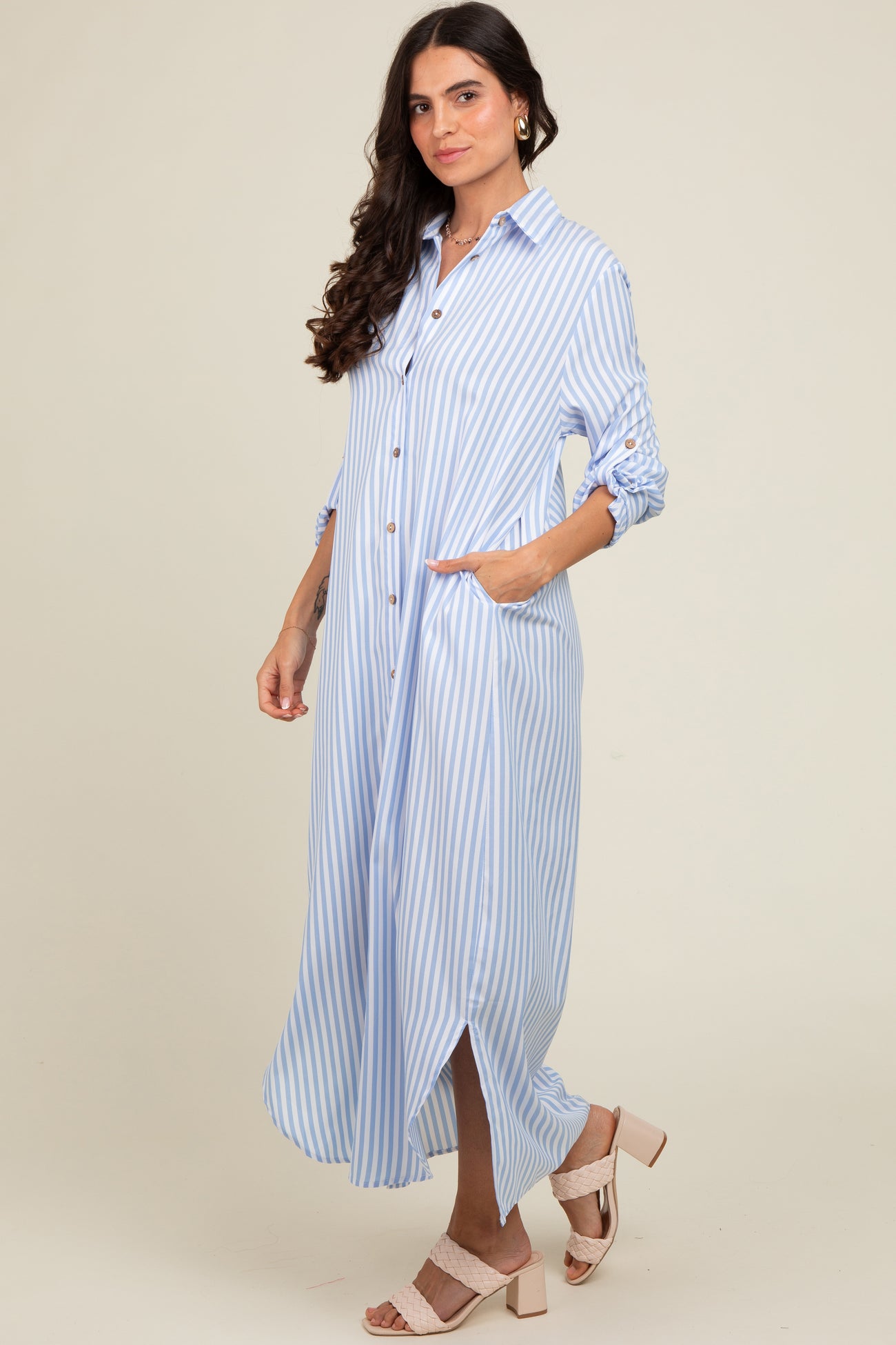 woman wearing a light blue and white striped button-up maxi dress with roll-up sleeves and pockets