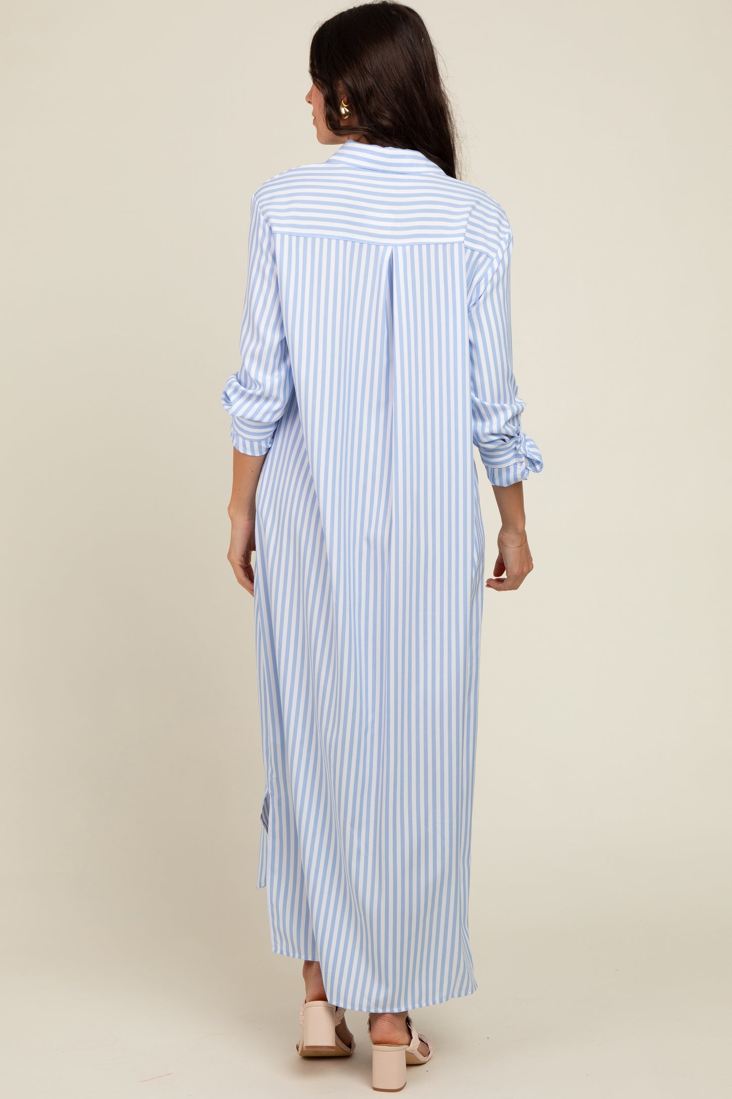 woman wearing a light blue and white striped long shirt dress with rolled sleeves and a back slit, viewed from behind