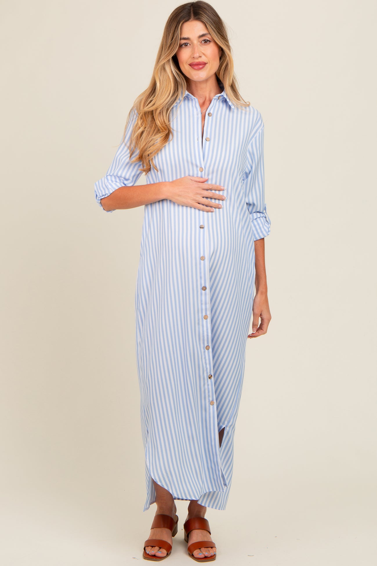 woman wearing a blue and white striped maternity maxi shirt dress, holding her baby bump with a casual smile