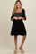 woman wearing a black maternity dress with embroidered details and a tiered skirt, smiling at the camera