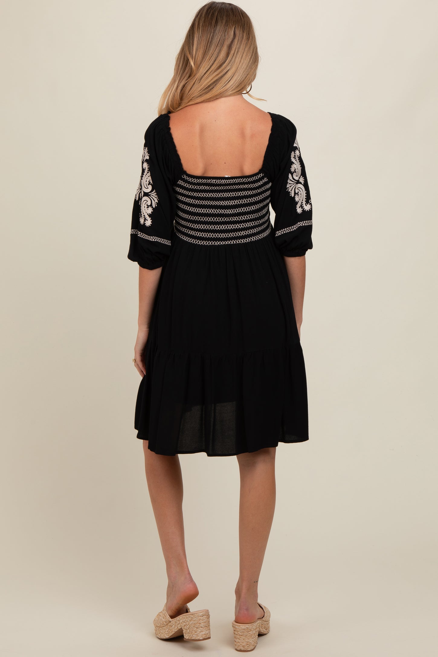 woman wearing a black maternity dress with embroidered sleeves and a fitted bodice, showing a relaxed, flowy skirt