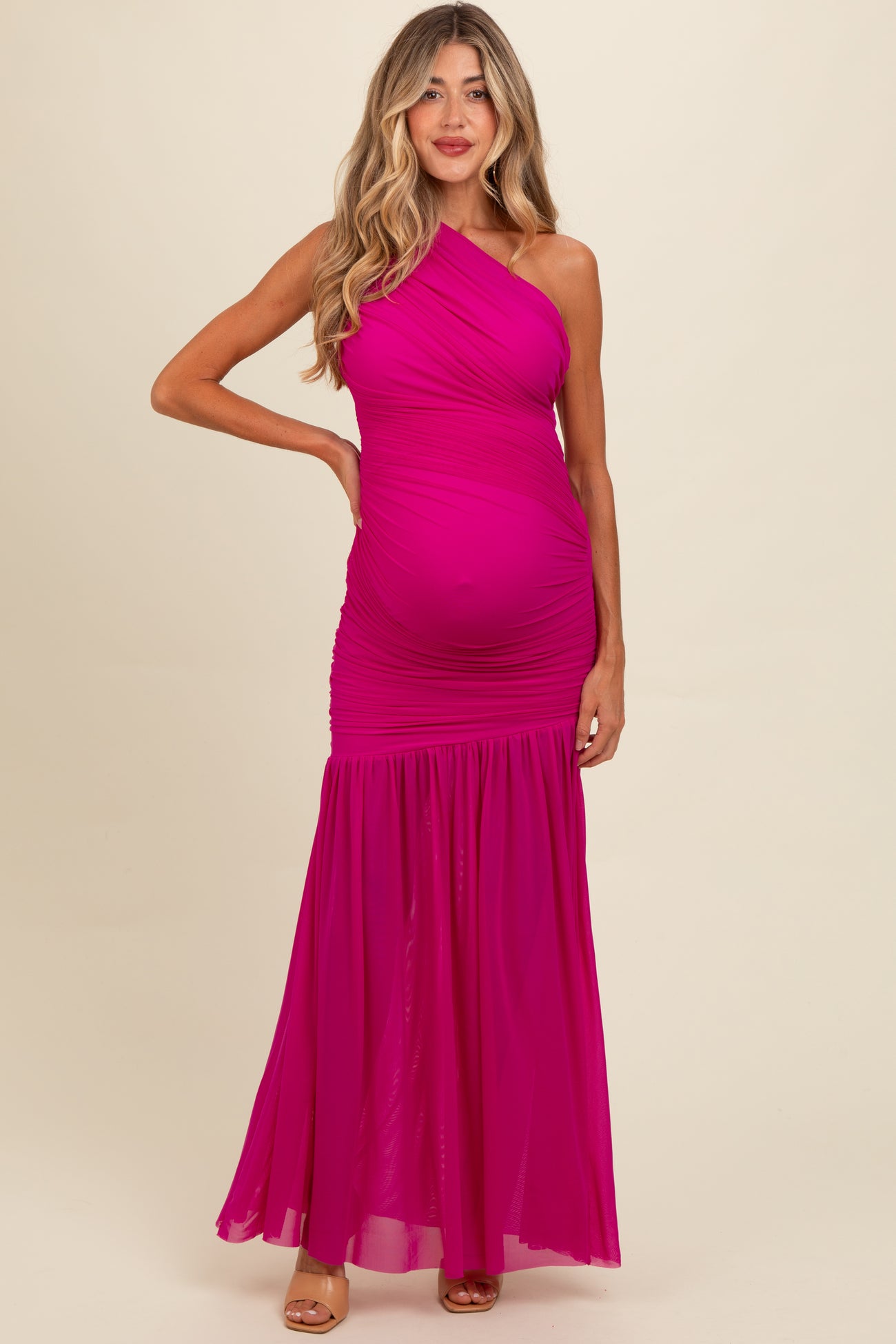 woman wearing a bright pink one-shoulder maternity gown with ruched details and a flowing skirt, showcasing her baby bump