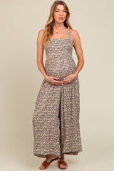 woman wearing a floral print maternity jumpsuit with adjustable straps and holding her baby bump