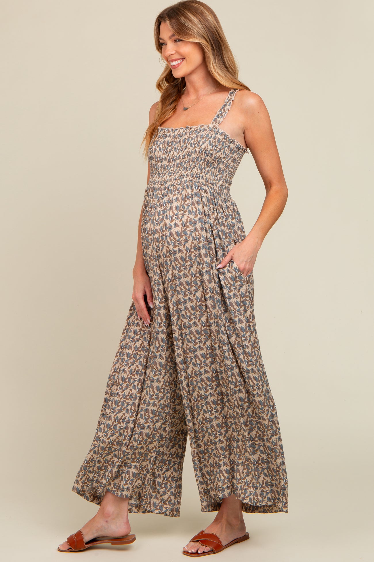 woman wearing a floral patterned maternity jumpsuit with a smocked bodice and wide-leg pants, showing her baby bump