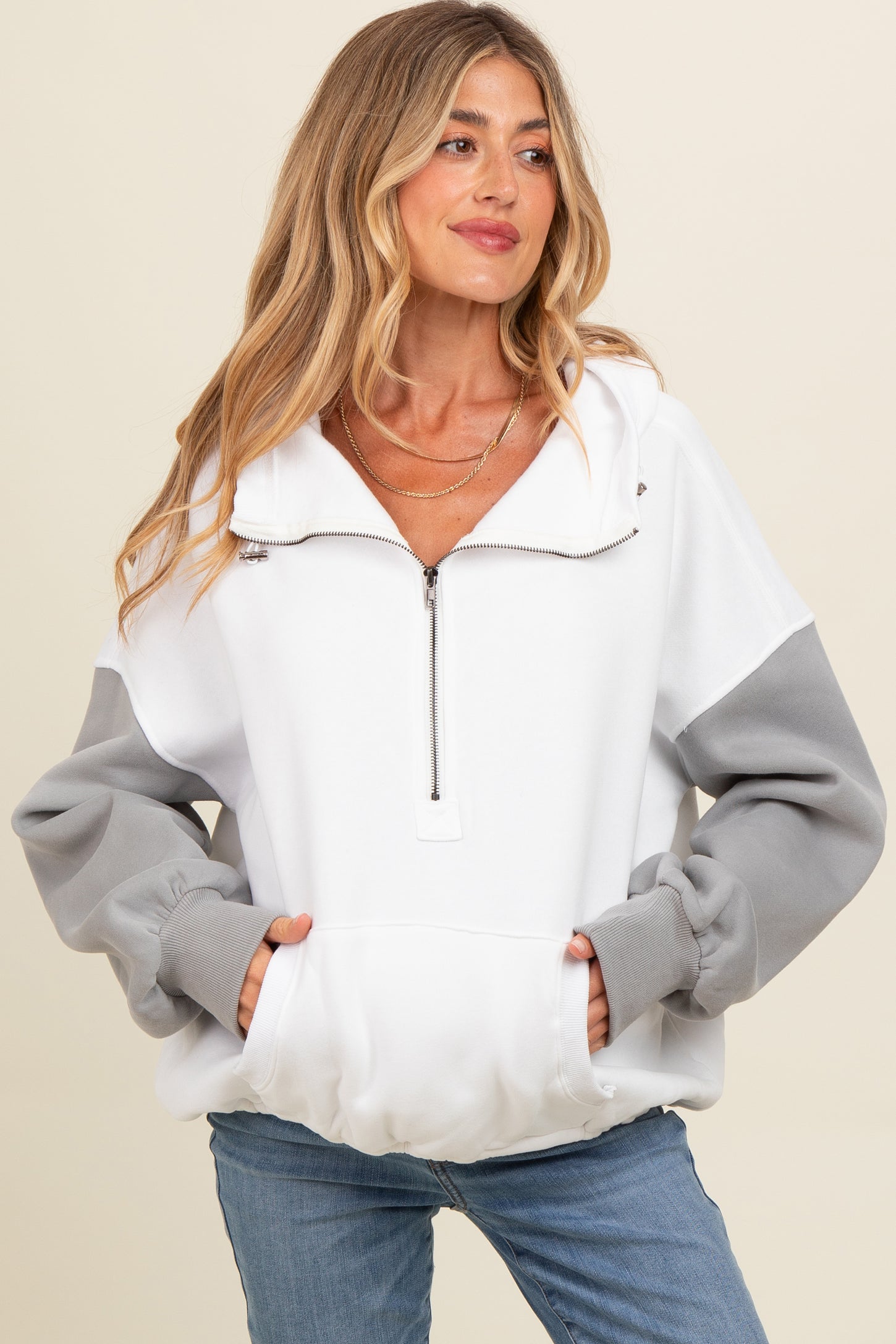 woman wearing a white and grey color block maternity sweatshirt with a half zipper and front pockets