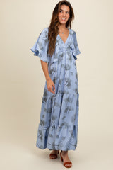 woman wearing a light blue floral maxi dress with flutter sleeves and a tiered skirt, smiling against a neutral background