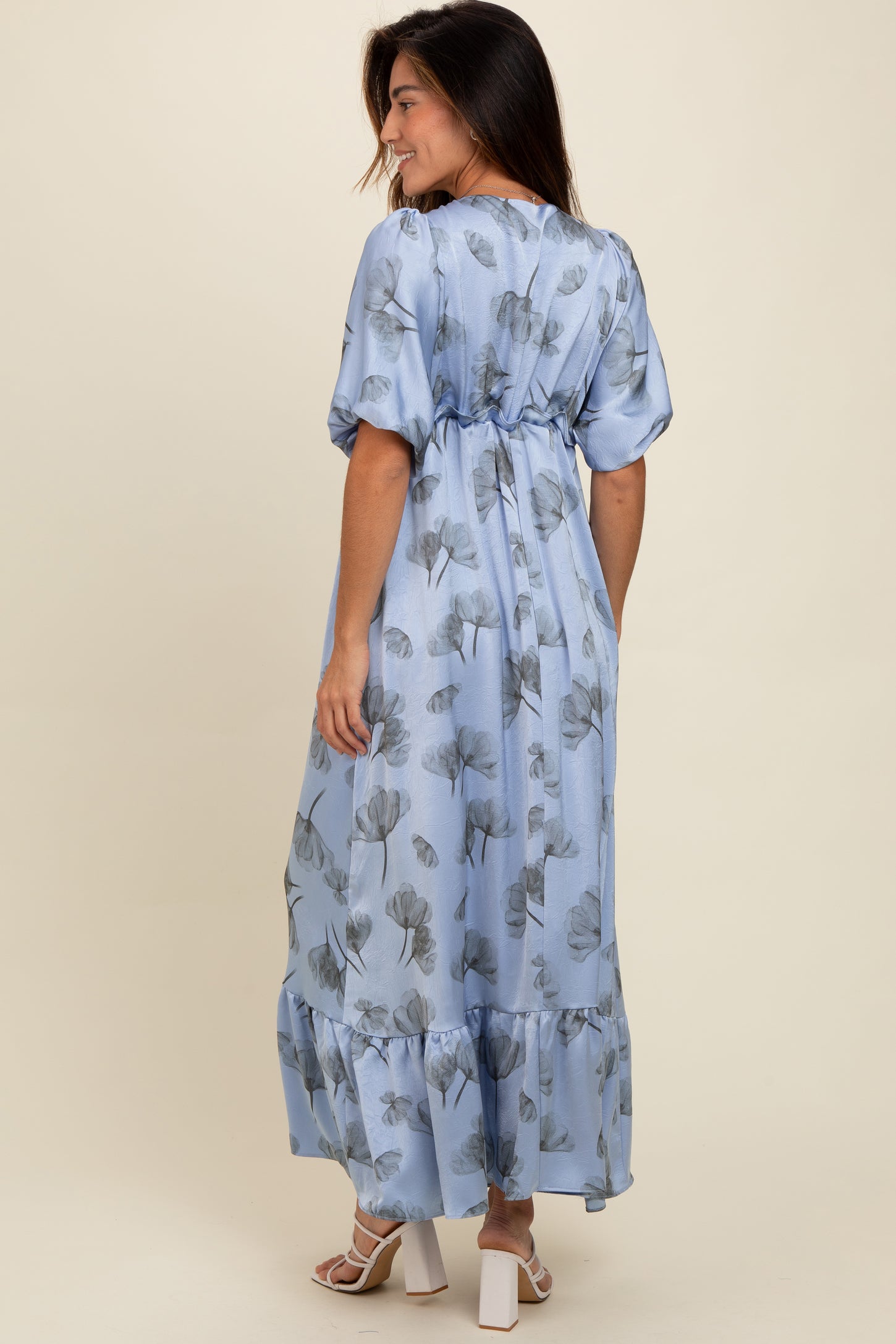 woman wearing a light blue floral maxi dress with puff sleeves and a tiered hem, facing away from the camera