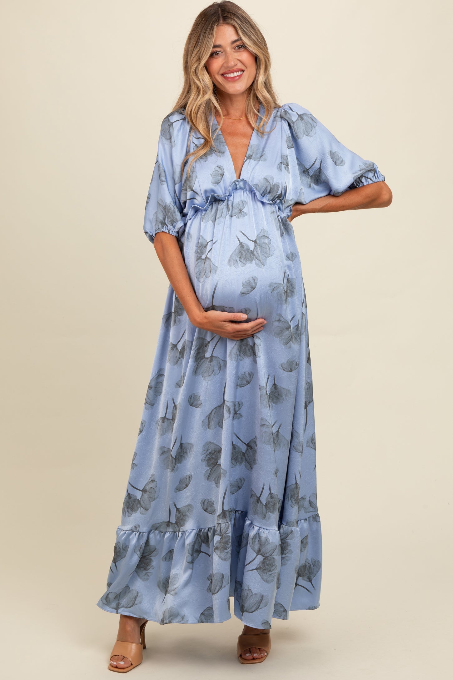 woman wearing a light blue maternity maxi dress with puff sleeves and floral print, holding her baby bump