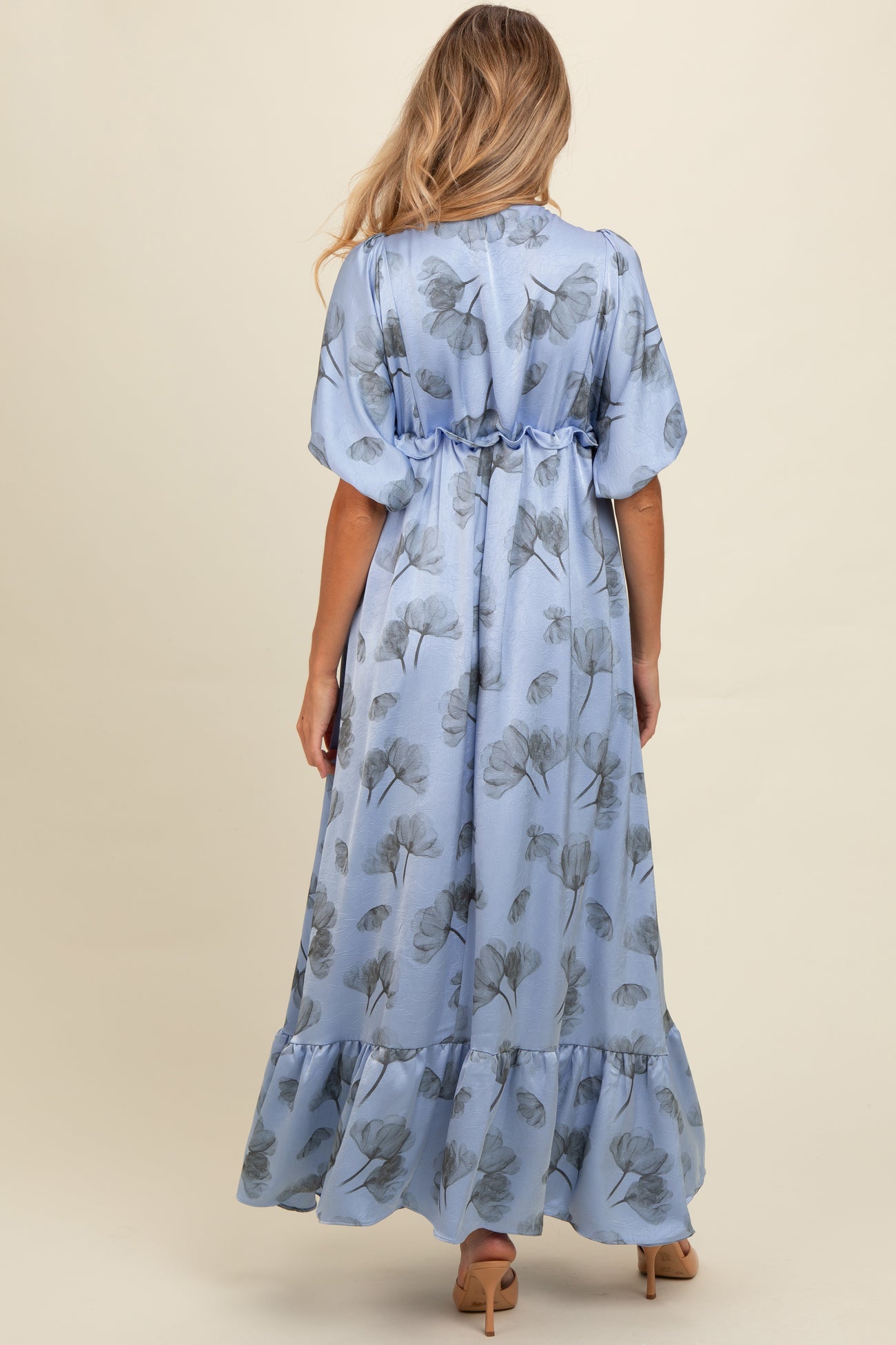 woman wearing a blue floral maternity maxi dress with a ruffled hem and cinched waist, showing her baby bump from the back