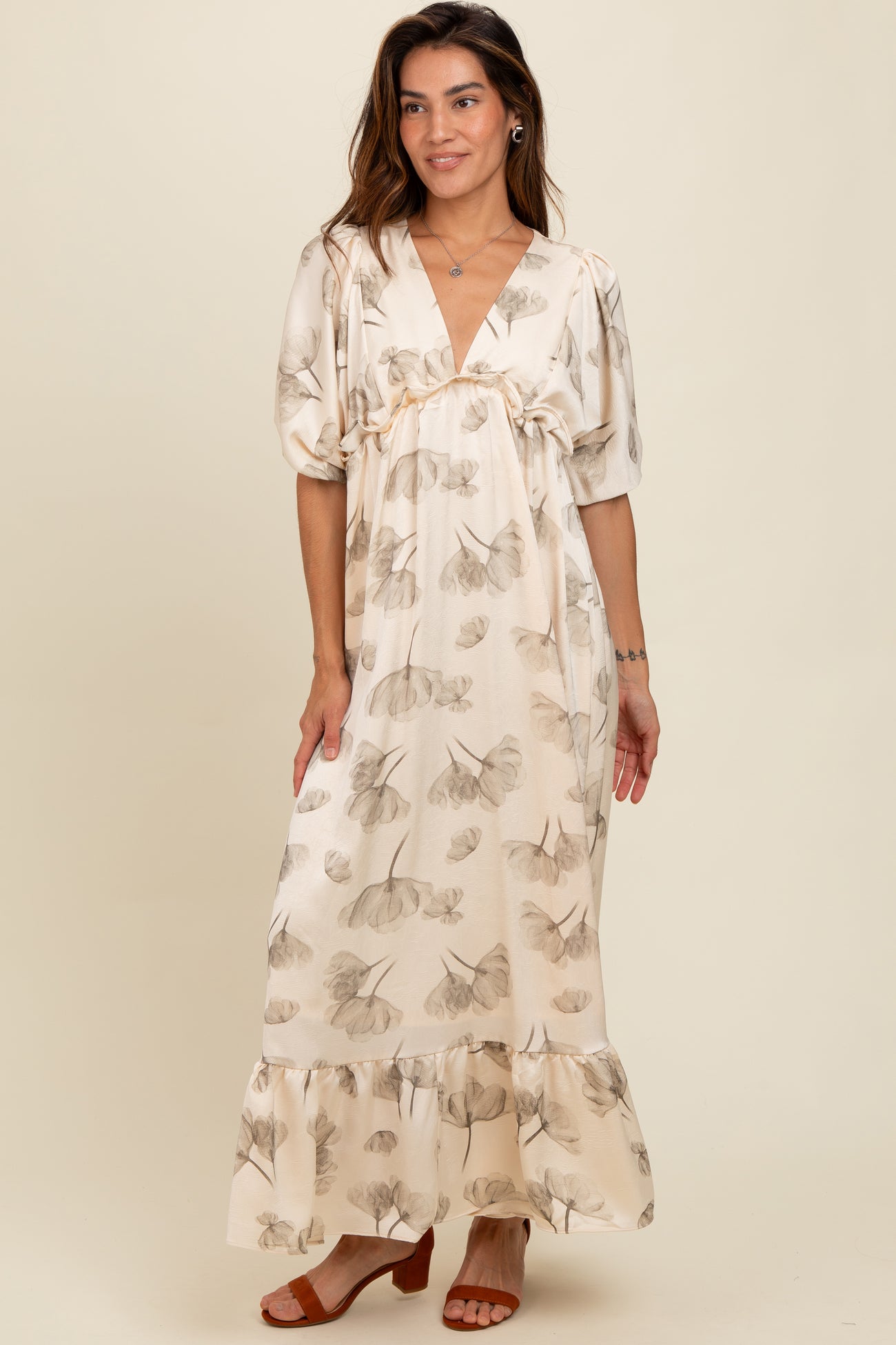 woman wearing a cream floral maxi dress with puff sleeves and a ruffled hem, standing on a neutral background